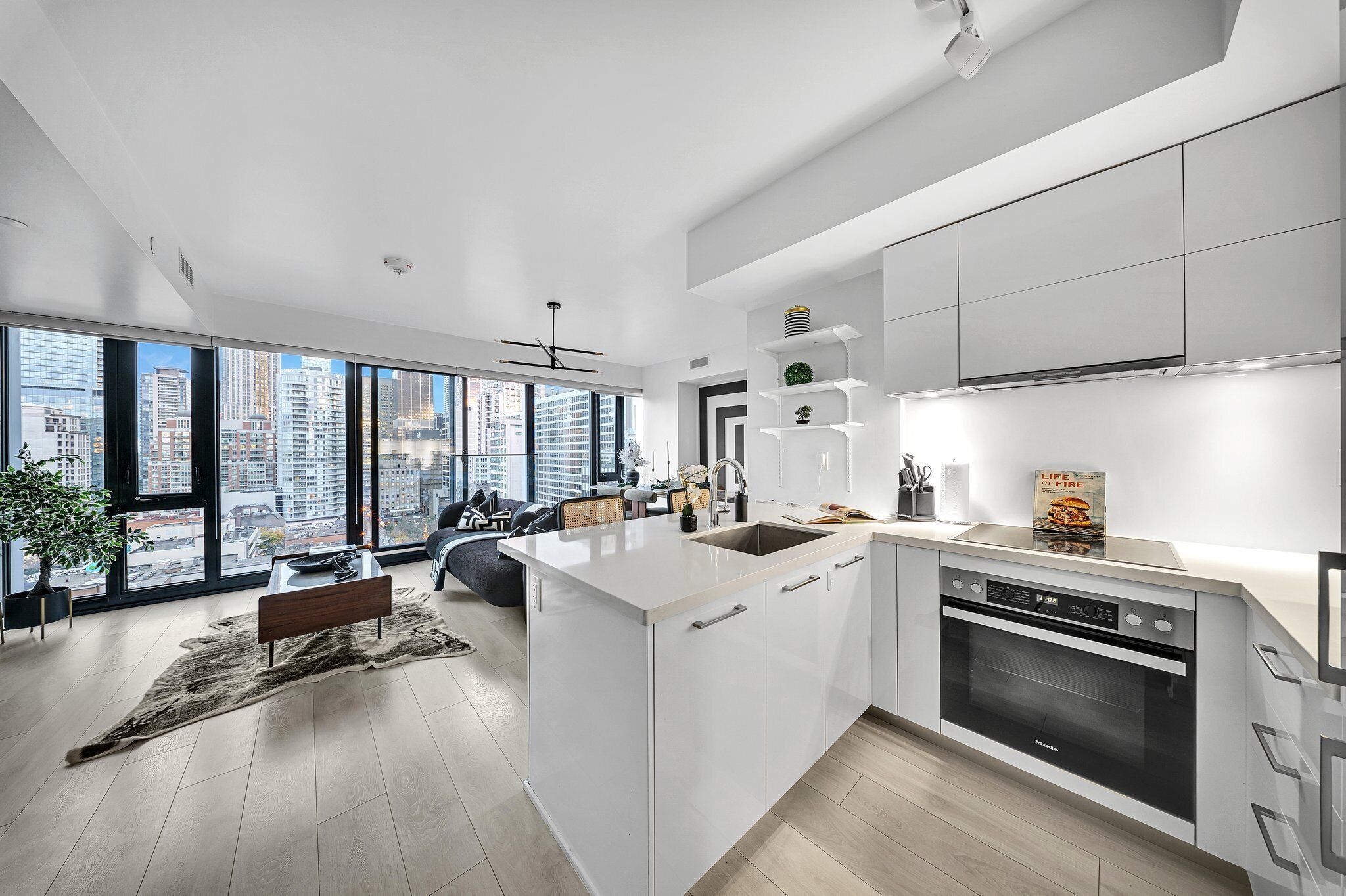 Een moderne keuken met een groot eiland, een inbouwoven en een stadszicht door grote ramen.