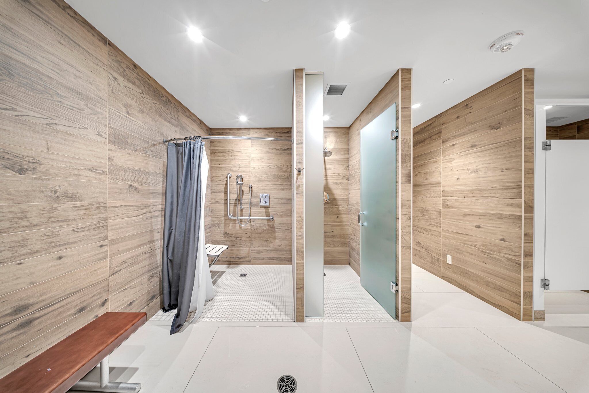 A modern bathroom with wooden walls, a glass shower enclosure, and a bench.