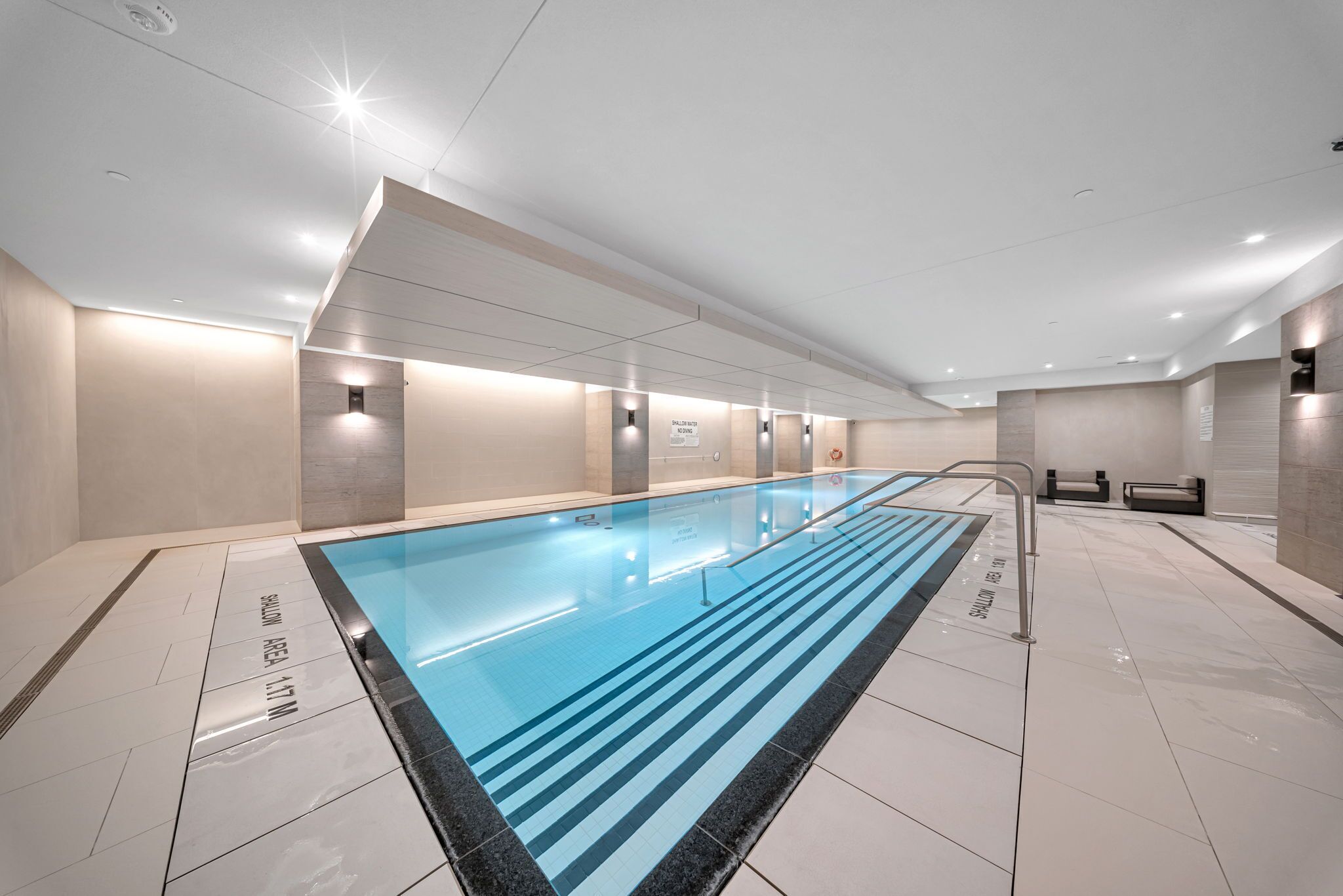Een modern binnenzwembad met duidelijke baanmarkeringen, een betegelde vloer en een plafond met ingebouwde verlichting.