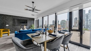 A modern dining area with a large table set for four, a blue sofa, and a city view through large windows.