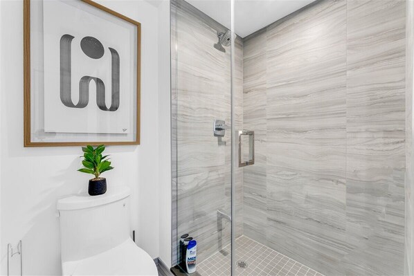 A bathroom with a toilet, a framed artwork, a potted plant, and a shower with a glass door.