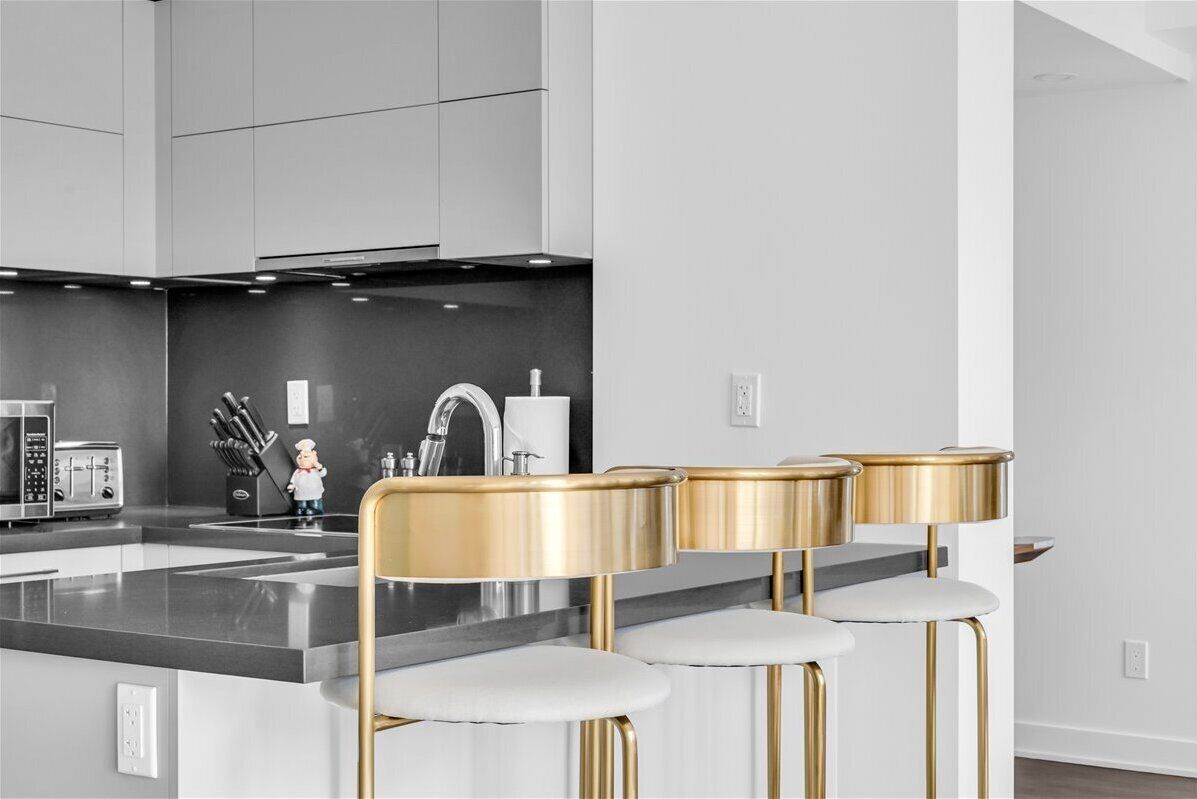 A modern kitchen with a central island, stainless steel appliances, and gold bar stools.