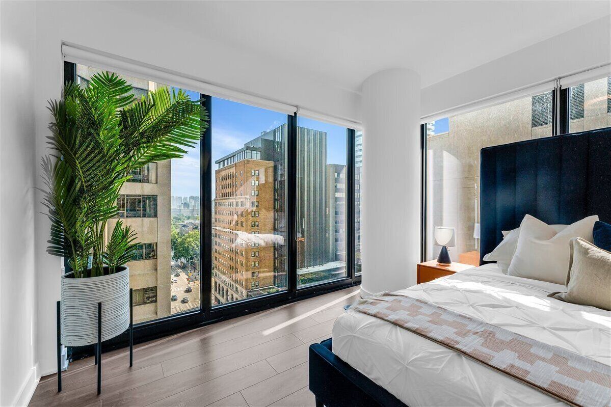 Quarto moderno com uma grande janela, um vaso de planta, uma cama com cabeceira azul e uma mesa de cabeceira com abajur.