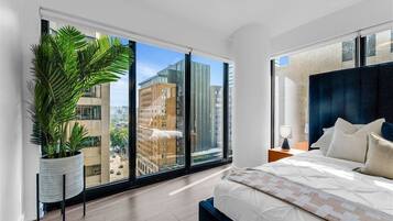 Quarto moderno com uma grande janela, um vaso de planta, uma cama com cabeceira azul e uma mesa de cabeceira com abajur.