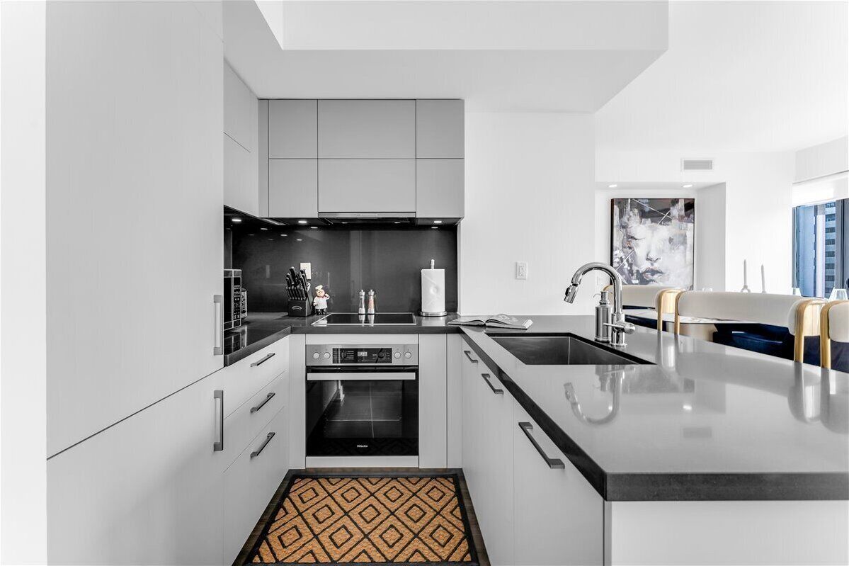 A modern kitchen with white cabinetry, a central island with a sink, and a built-in oven.