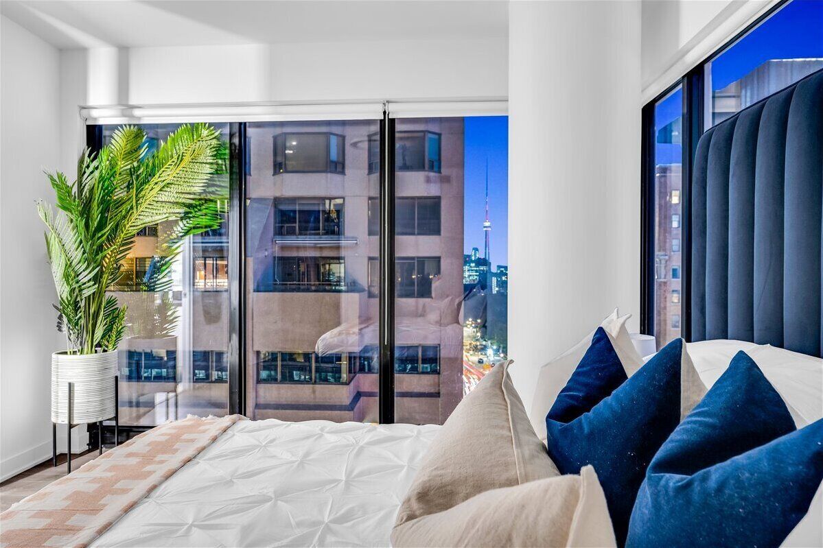 Ein modernes Schlafzimmer mit einem großen Fenster, einer Topfpflanze und einem Bett mit blau-weißen Kissen.
