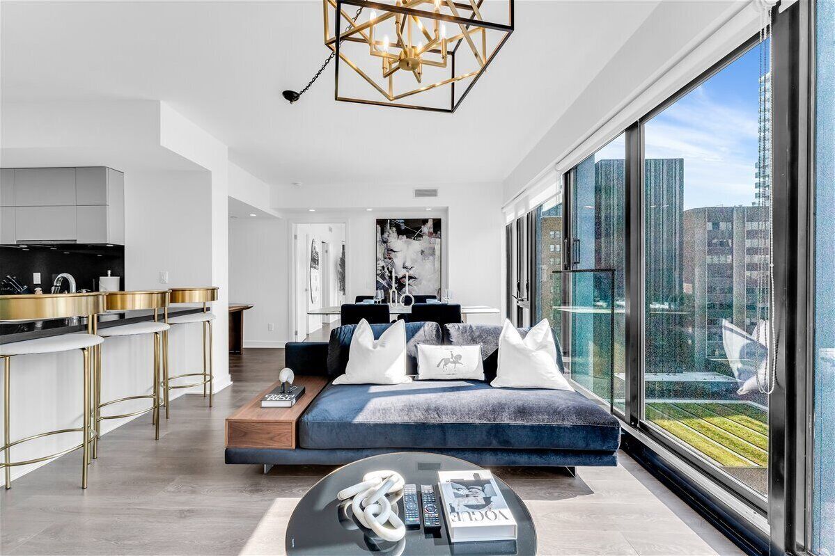 A modern living room with a sofa, a coffee table, and a view of the city through large windows.
