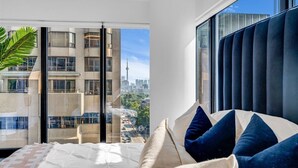 A modern hotel room with a large bed, a view of the cityscape, and a sliding glass door to the outside.