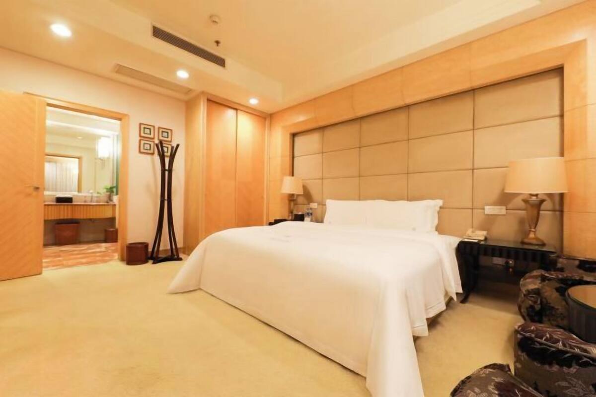 Ein Hotelzimmer mit einem großen Bett, Nachttischen, einem Spiegel und einer Tür zu einem Badezimmer.
