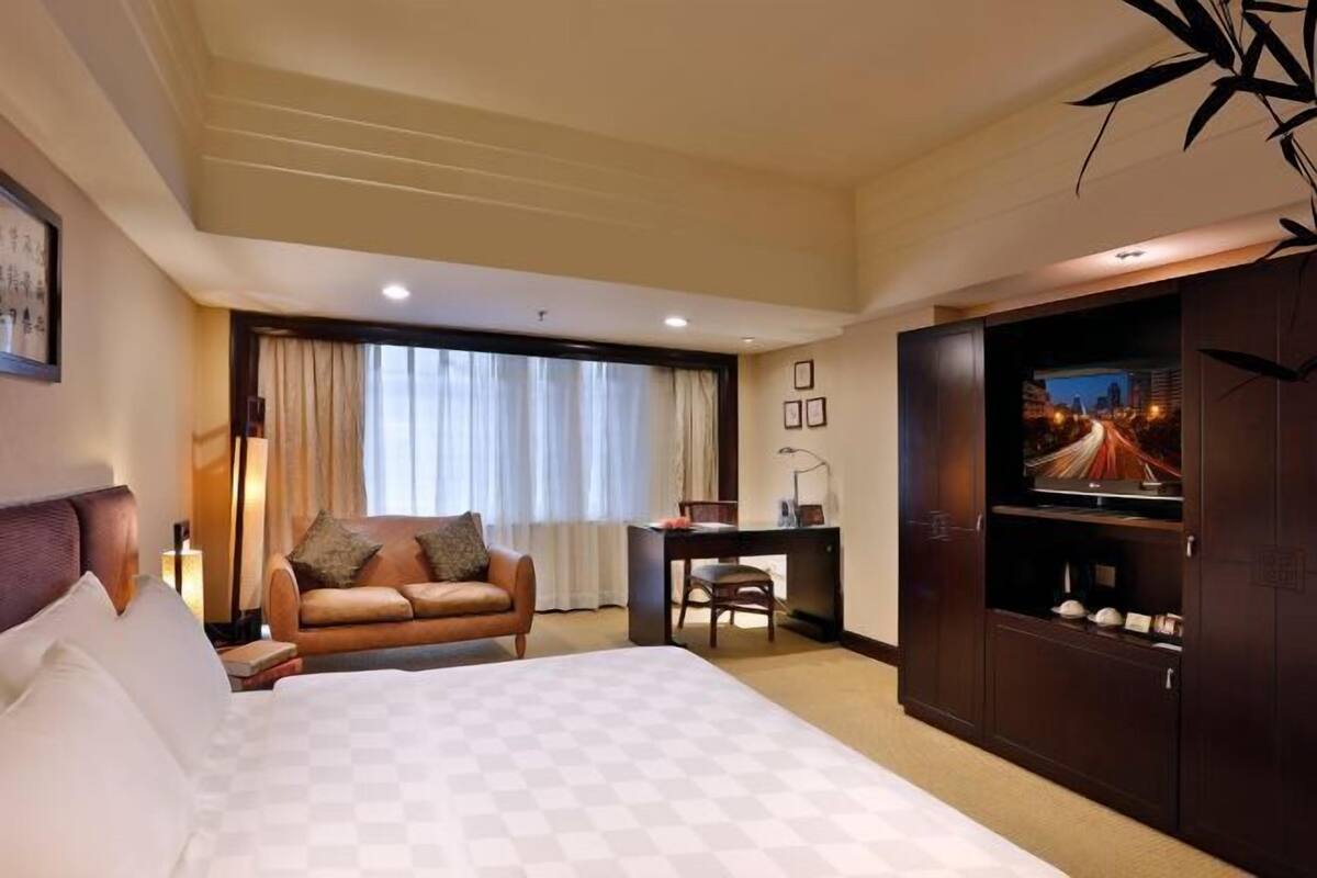 Ein Hotelzimmer mit einem großen Bett, einem Schreibtisch, einer Couch und einem Fernseher auf einem Schrank.
