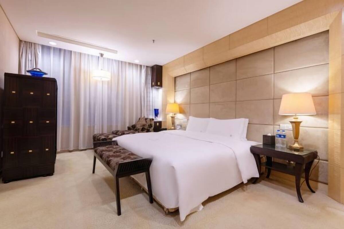 Ein Hotelzimmer mit einem großen Bett, einem Schreibtisch, einem Stuhl, einem Kleiderschrank und einem Fenster mit Vorhängen.