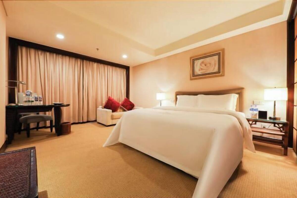 Ein Hotelzimmer mit einem großen Bett, einem Schreibtisch mit Stuhl, einer Lampe und einem Bild an der Wand.