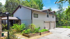 A two-story house with a garage, a front porch with a bench, and a landscaped garden with various plants and a wooden planter. - Cloud 9 -- Cozy studio with WiFi, AC in charming Chuluota, FL (Chuluota)
