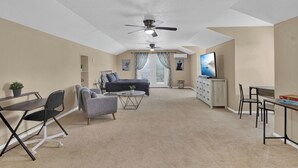 A spacious living room with a sofa, armchairs, a coffee table, and a TV. There is a ceiling fan, a window with curtains, and a door leading to another room. - Cloud 9 -- Cozy studio with WiFi, AC in charming Chuluota, FL (Chuluota)