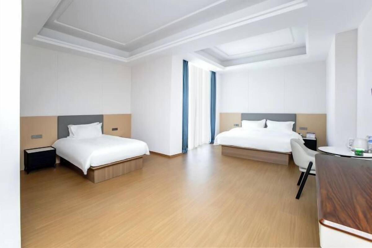 Hotellihuone, jossa on kaksi sänkyä, työpöytä, tuoli ja ikkuna, jossa on verhot.