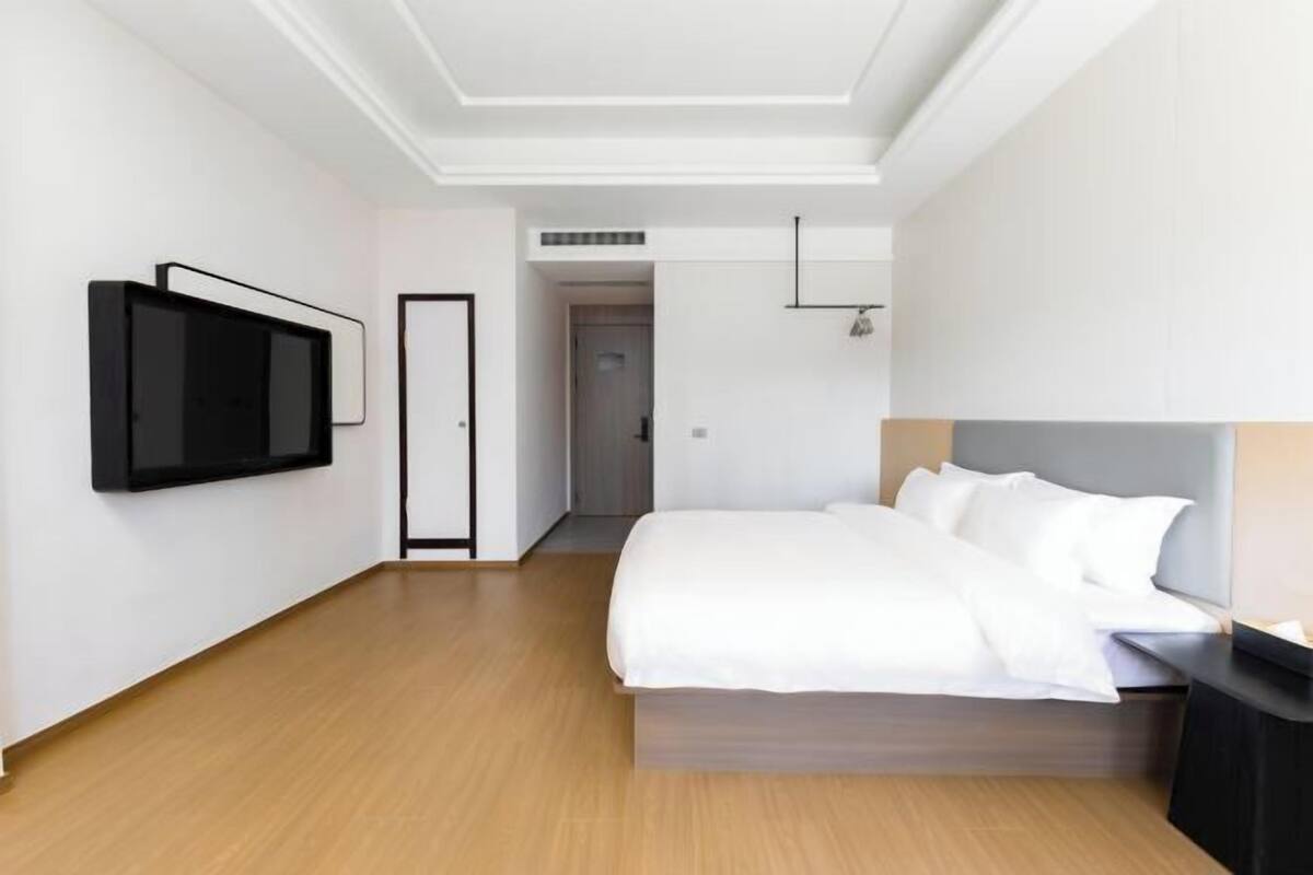 Moderni hotellihuone, jossa on suuri sänky, seinälle asennettu taulutelevisio ja pelkistetty sisustus.
