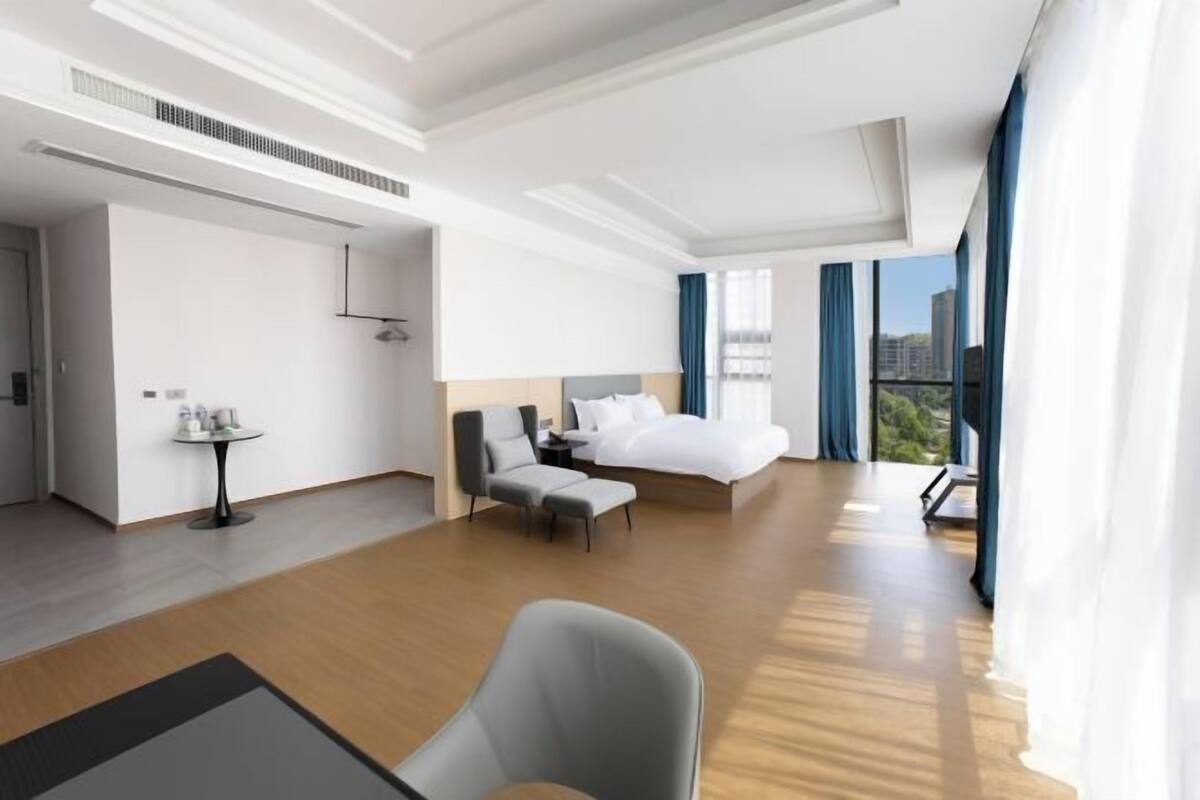 Moderni hotellihuone, jossa on suuri sänky, oleskelualue, pieni pöytä ja näkymä kaupunkiin.