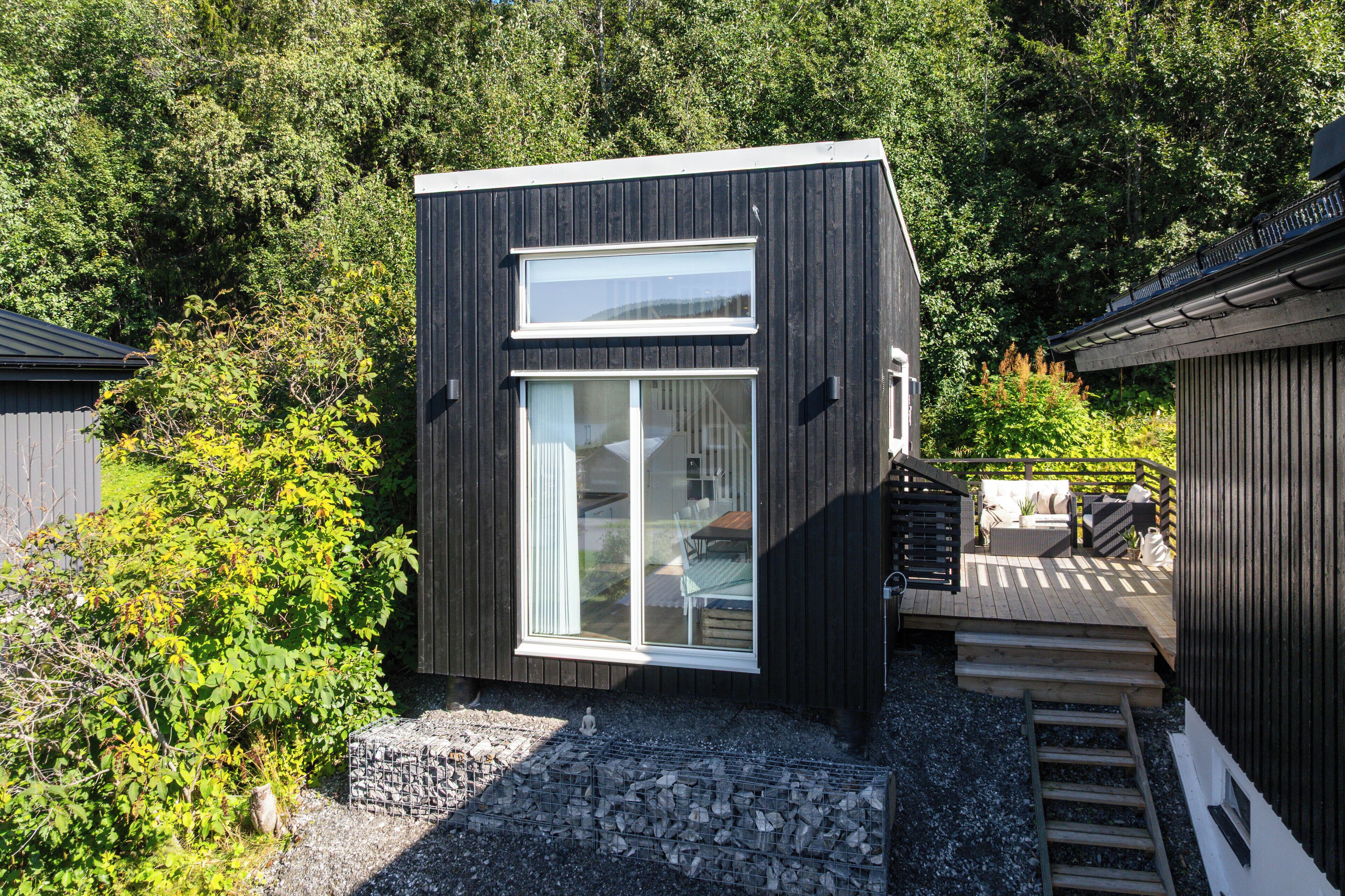 A modern, compact building with a large glass window, surrounded by dense greenery.