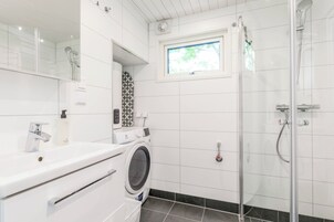 Un baño moderno con lavadora integrada, cabina de ducha y ventana que proporciona luz natural.