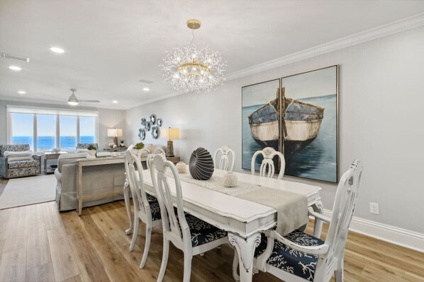A dining area with a white table and chairs, a chandelier, and a large painting of a boat on the wall.