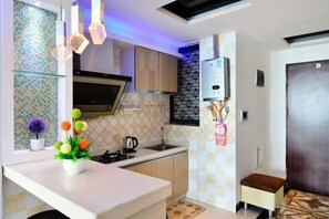 A modern kitchen with a white countertop, a built-in oven, and a microwave. There is a small stool and a potted plant on the counter. - Beihai Beibu Gulf No.1 Yazhijia Scenic Apartment (Beihai)