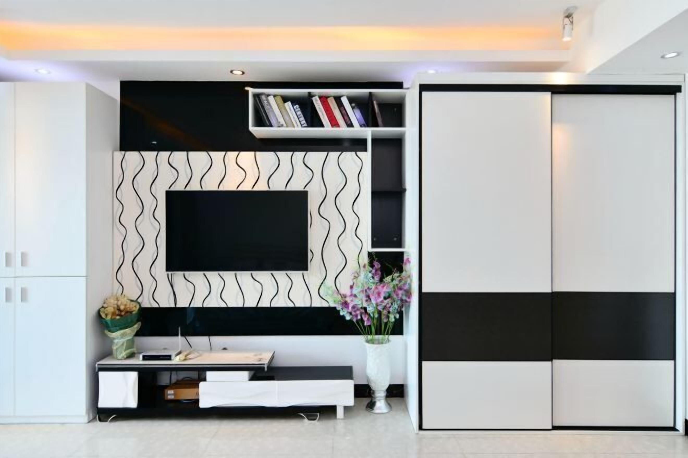 A modern living room with a flat-screen TV mounted on a wavy-patterned wall, a white console table with a vase of flowers, and a sliding closet door.