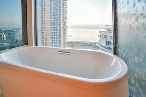 A modern bathroom with a freestanding bathtub, large windows offering a view of a cityscape and the sea. - Beihai Beibu Gulf No.1 Yazhijia Scenic Apartment (Beihai)