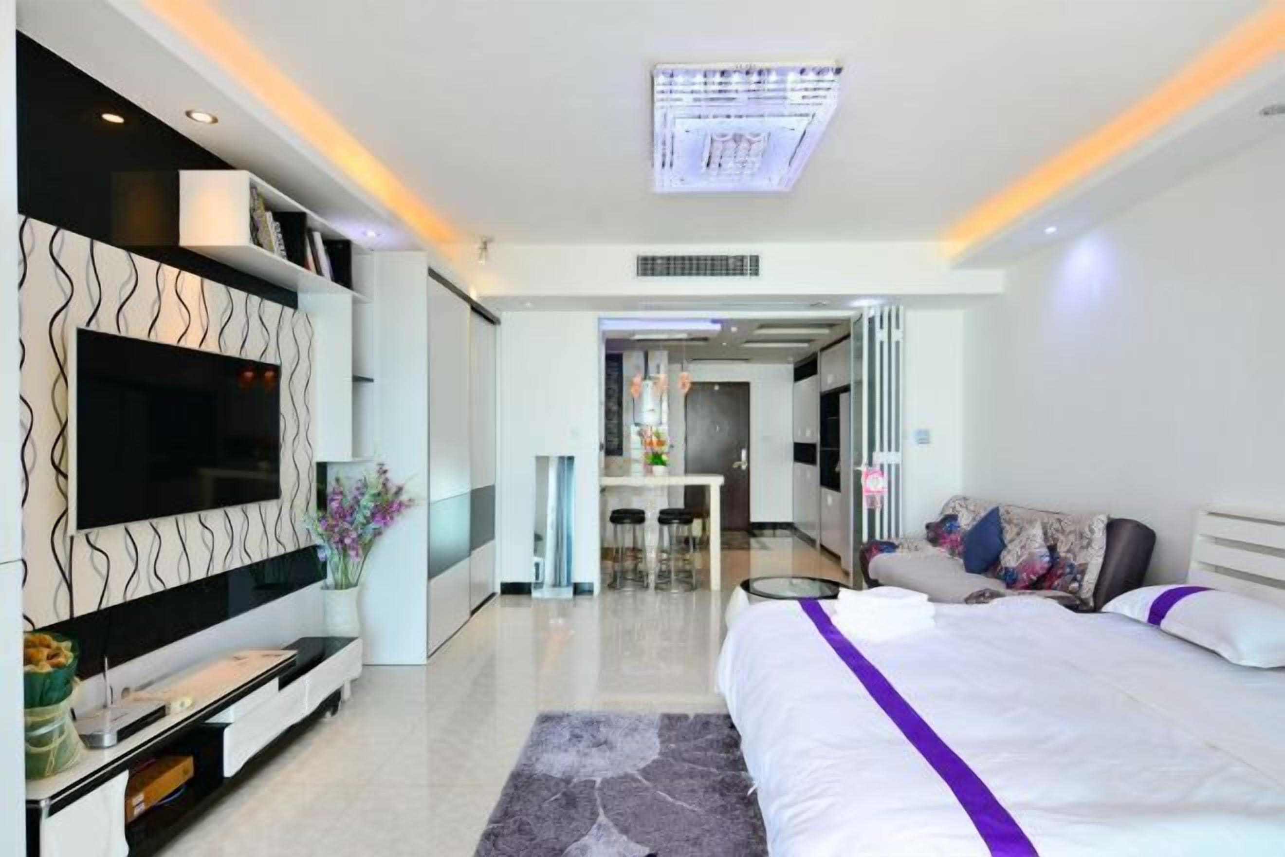 Una habitación de hotel moderna con una cama grande, un televisor de pantalla plana, una zona de comedor y un baño visible a través de una puerta abierta.