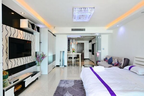 A modern hotel room with a large bed, a flat-screen TV, a dining area, and a bathroom visible through an open door. - Beihai Beibu Gulf No.1 Yazhijia Scenic Apartment (Beihai)