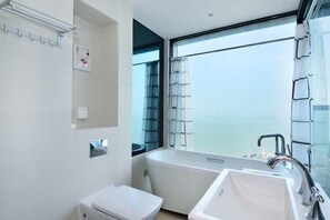 A modern bathroom with a bathtub, a toilet, and a sink. There is a window providing a view of the outdoors. - Beihai Beibu Gulf No.1 Yazhijia Scenic Apartment (Beihai)