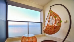 Ein Zimmer mit großem Fenster und Blick auf ein Gewässer, einem Hängekorbstuhl und einem kleinen Tisch.