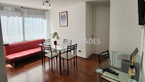 Ein modernes Wohnzimmer mit einem roten Sofa, einem Glastisch mit Stühlen, einem kleinen Topfpflanzen und einem Laptop auf einem Glastisch.