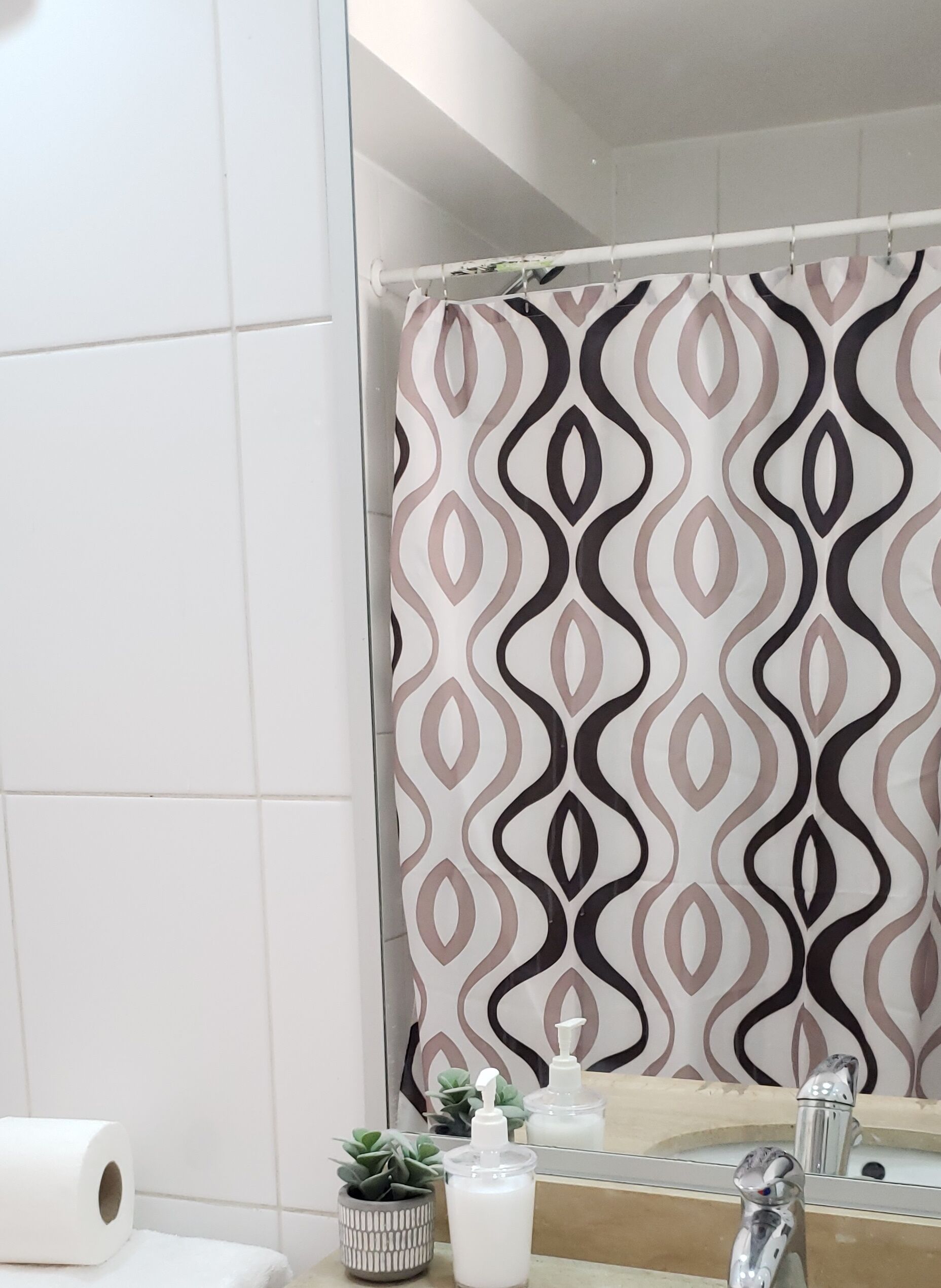 Een badkamer met een douchegordijn met een geometrisch patroon, een toiletpapierrol, een kleine potplant en een zeepdispenser.