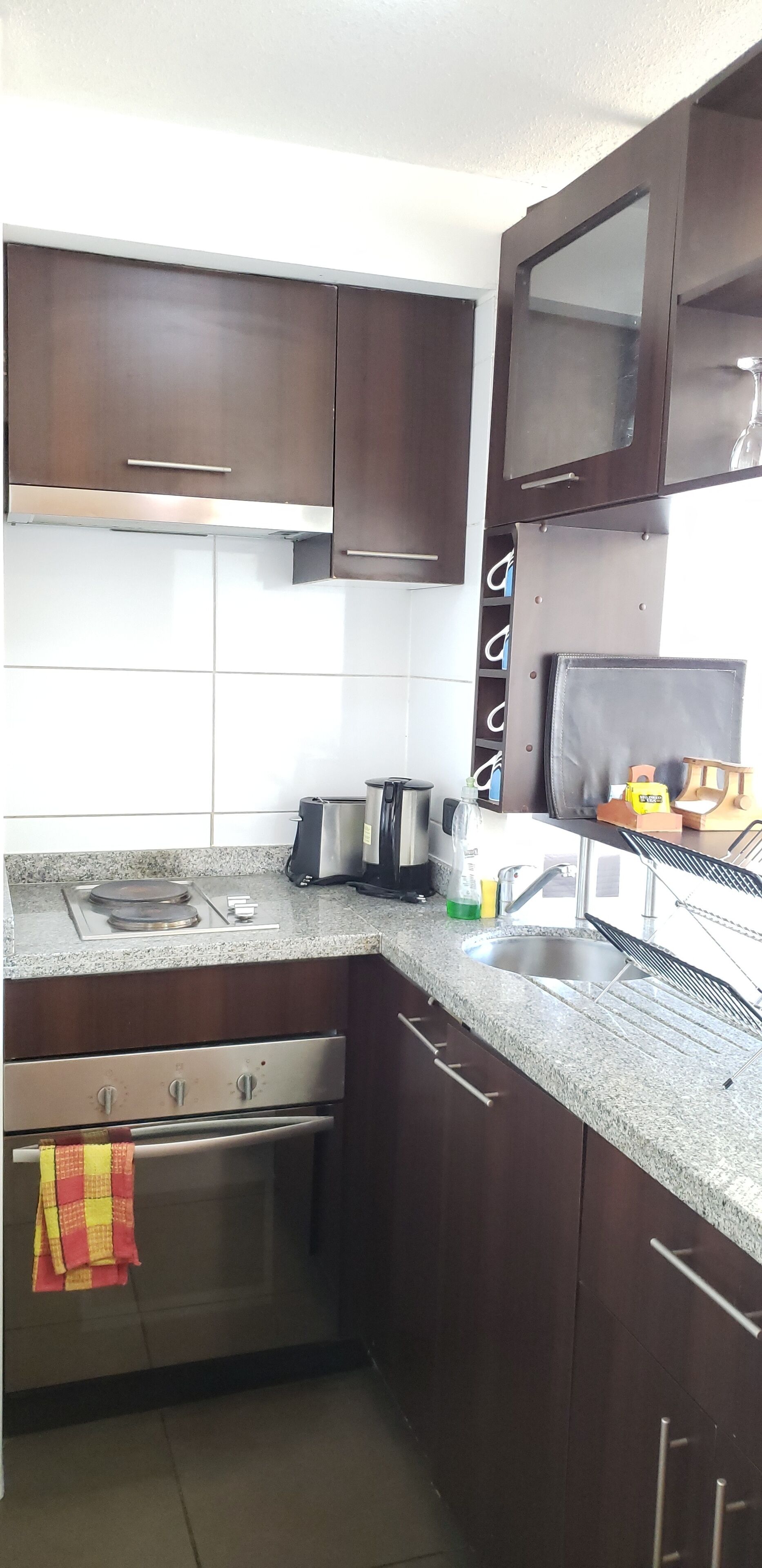 Eine Küche mit dunklen Holzschränken, einer Edelstahl-Dunstabzugshaube, einer Granit Arbeitsplatte, einem Einbauofen und einem Spülbecken.