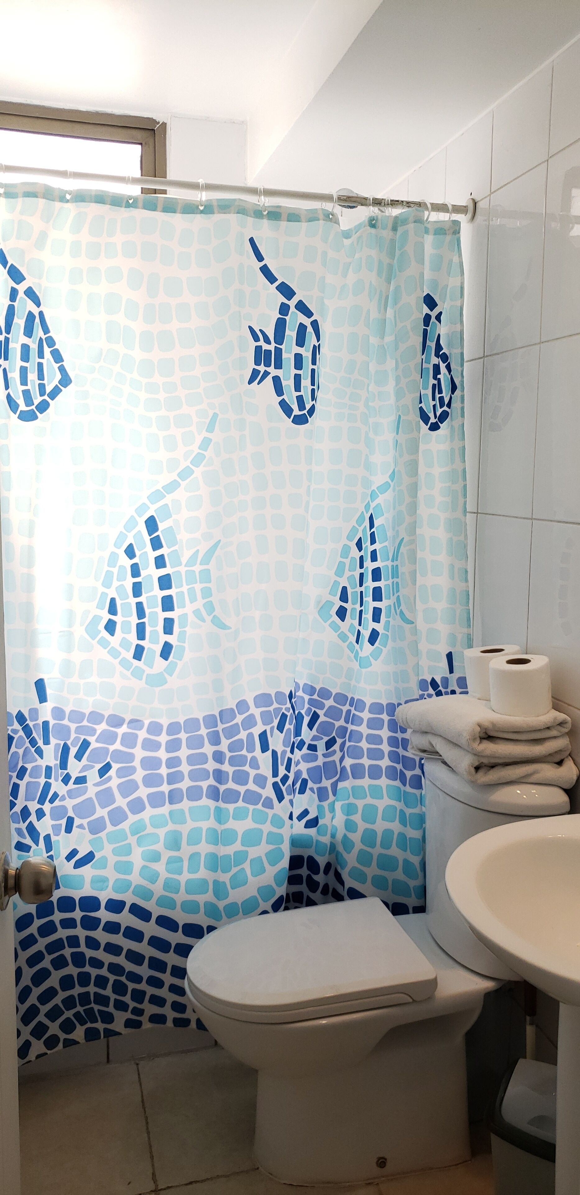 A bathroom with a shower curtain featuring a mosaic pattern of fish, a toilet, and a sink with stacked towels.