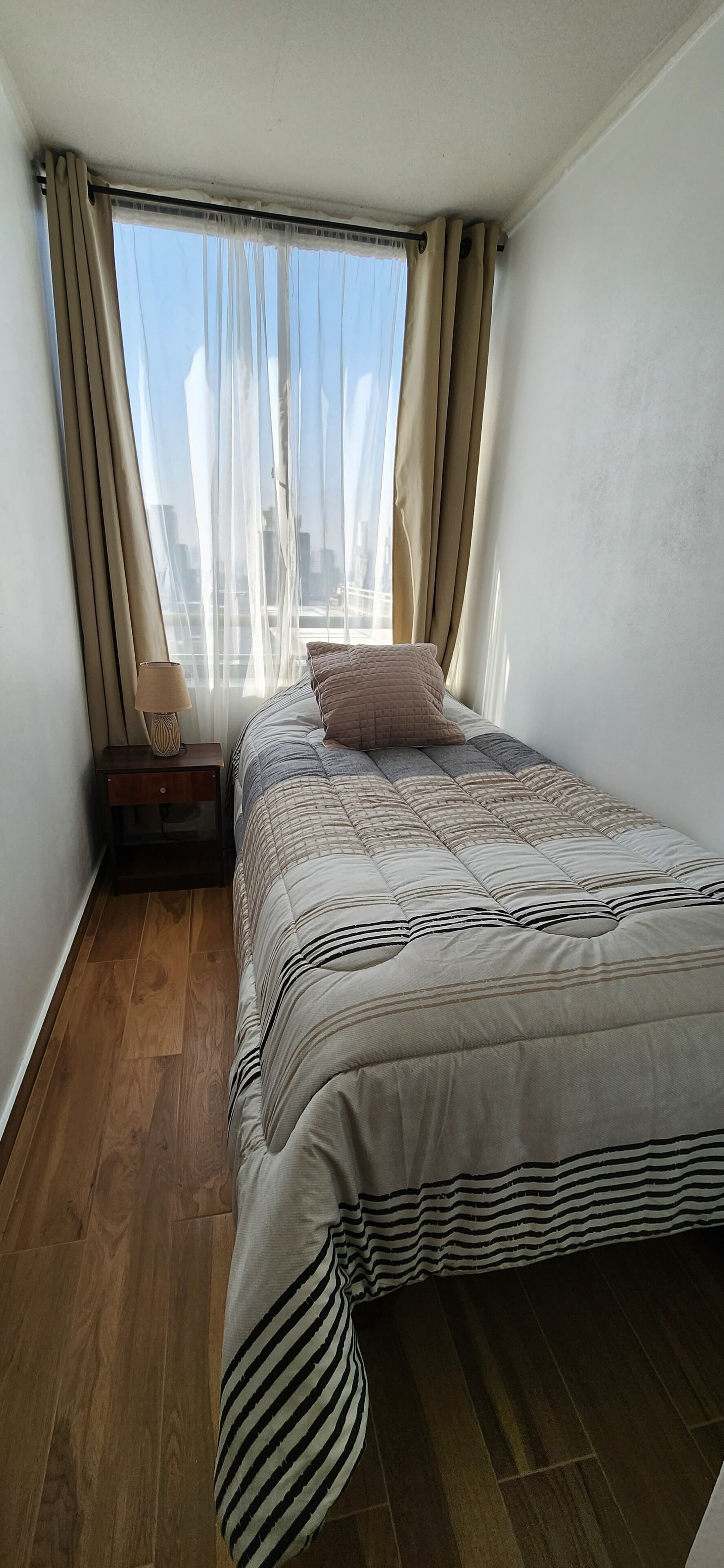 A bedroom with a bed, a nightstand, a lamp, and a window with curtains.