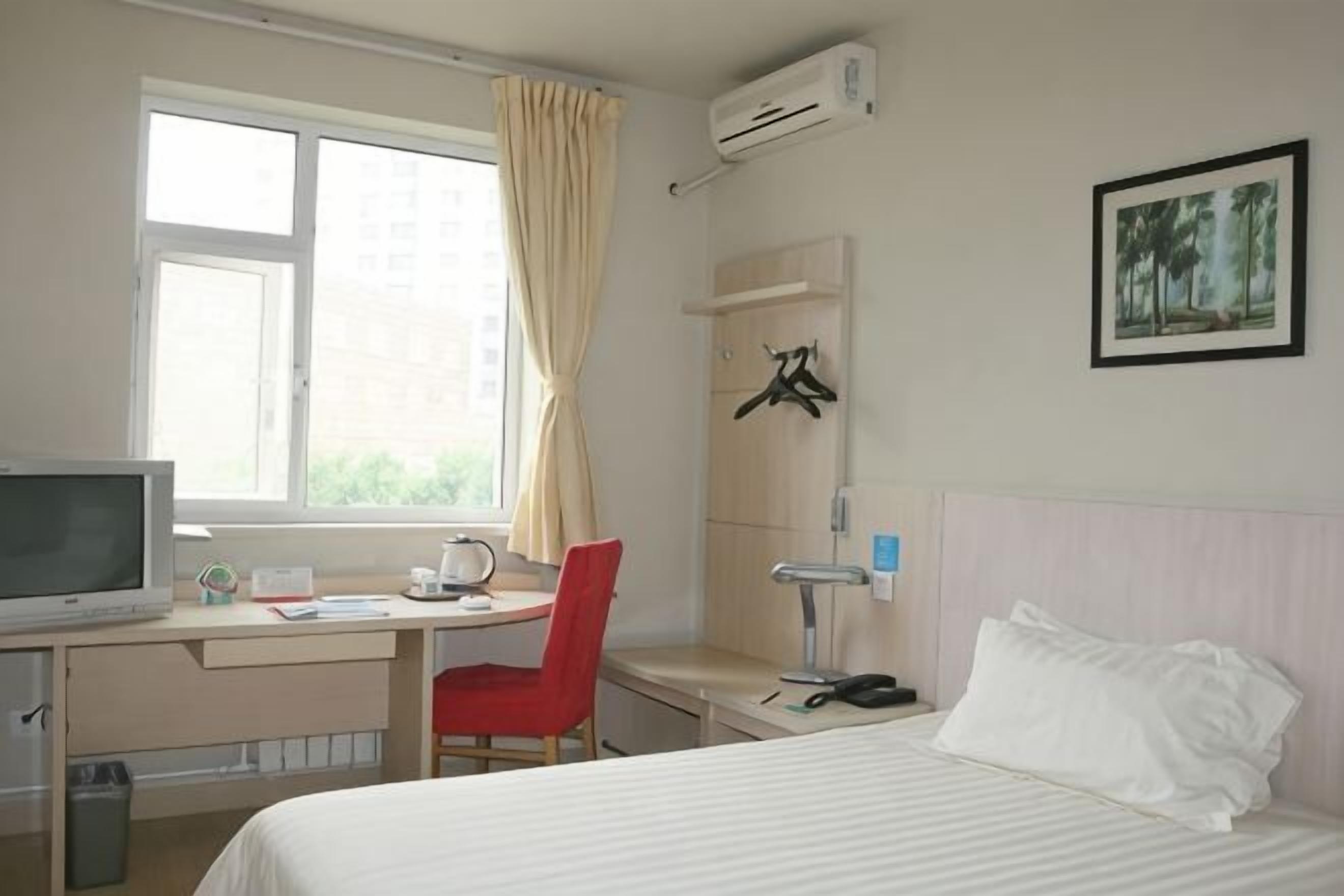 Una camera d'albergo con un letto, una scrivania, una sedia, una TV e una finestra con tende.