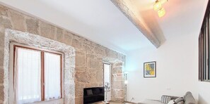 A room with a stone wall, a sliding door, a black sofa, a standing fan, and a framed picture on the wall. - N&J - VILLA FAY - Promenade - Near Beach (Niza)