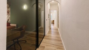 Un corridoio con pavimento in legno, un divisorio in vetro e una sala da pranzo con tavolo e sedie.