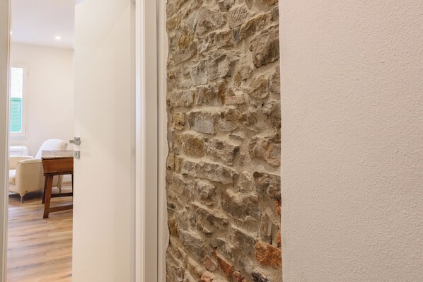 A hallway with a stone wall, a wooden floor, and a white door leading to a room with a bed and a chair. - Fiammetta by Mmega (Florence)