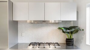 Une cuisine moderne dotée d’une cuisinière à gaz en acier inoxydable, de meubles blancs et d’un dosseret carrelé.