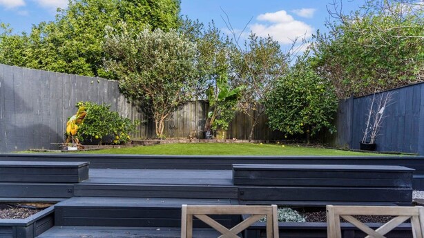 Un jardin avec une terrasse en bois, une mangeoire à oiseaux et une variété de plantes.