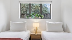 Une chambre avec deux lits, une table de chevet avec une lampe et une fenêtre agrémentée de plantes.