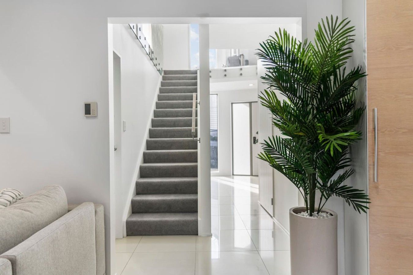 A modern interior with a staircase leading to an upper level, a potted plant, and a white sofa.