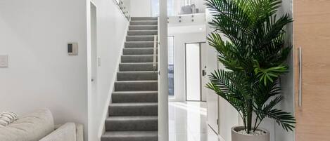 A modern interior with a staircase leading to an upper level, a potted plant, and a white sofa.
