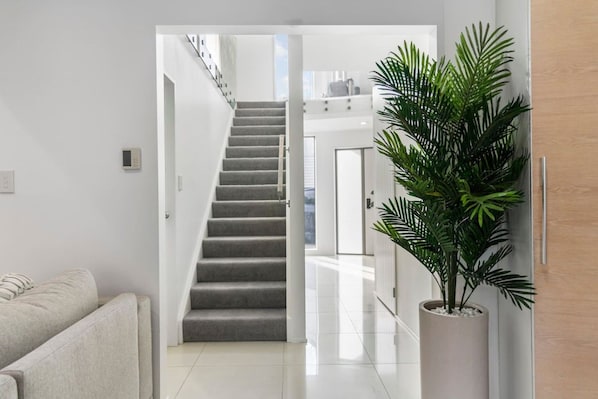 A modern interior with a staircase leading to an upper level, a potted plant, and a white sofa.