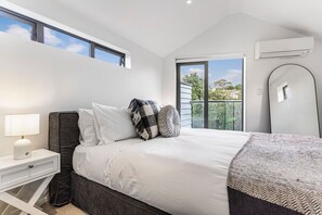 A bedroom with a bed, bedside table, lamp, and a view of the outside.