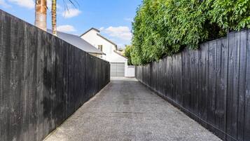 A narrow paved pathway flanked by dark wooden fences, leading to a white building with a garage.
