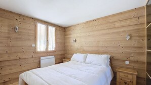 A wooden-paneled bedroom with a bed, a nightstand, and a window with curtains. - APARTMENT BALCONS DU MONT D'EVIAN - 8 PEOPLE - ST JEAN D'AULPS VILLAGE (Saint-Jean-d´Aulps)
