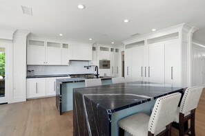 A modern kitchen with white cabinetry, a large island with a black marble countertop, and a built-in oven. - BEAUTIFUL never before seen golf course home in "THE GRAND" (Surprise)